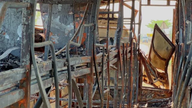 Panning shot inside a fire damaged sleeper bus showing twisted metal frames, charred compartments and rear emergency exit door in daylight!