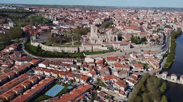 4K aerial drone shot approaching the historic old town of Zamora, Spain, featuring the Romanesque Cathedral, medieval castle ruins, and ancient walls on a bright sunny day.