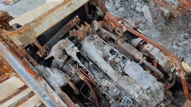Closeup of heavily burned bus engine compartment with ash covered machinery, rusted metal parts and severe fire destruction under daylight conditions!