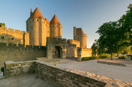 Medieval city walls and towers glow in golden hour light under a clear sky, an iconic European travel and tourism destination, Carcassonne, France.