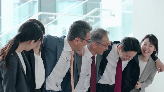 オフィスで肩を組んで笑うビジネスパーソンのグループ