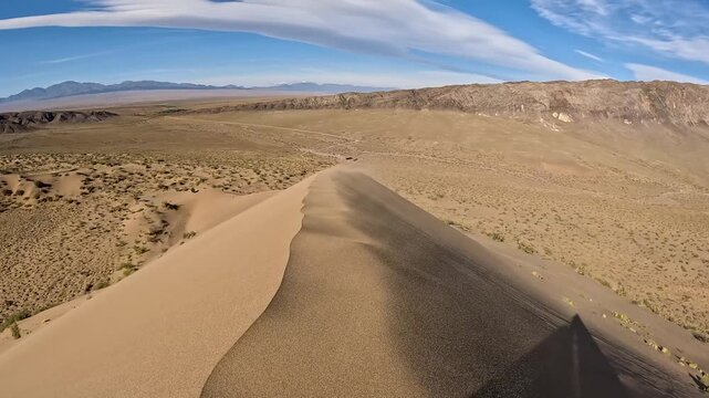 Close aerial view of wind-driven sand movement on a desert dune. Natural patterns and textures formed by moving sand.