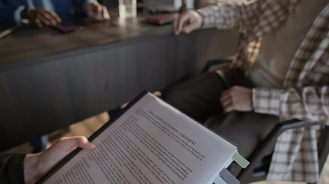 Pull out shot of brunette woman reading final divorce settlement agreement while her spouse and lawyer communicating in background