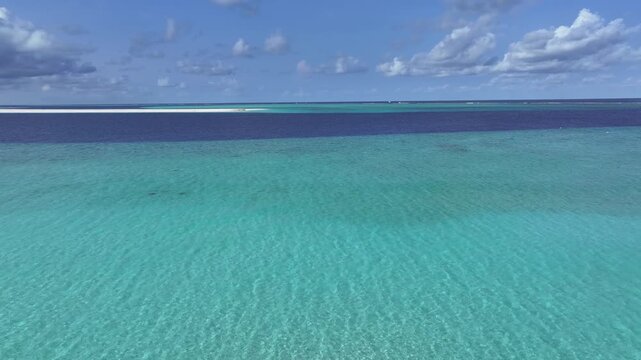 Aerial view of crystal clear turquoise lagoon water with a white sandbar under a blue sky with clouds in Gulhi, Kaafu Atoll, Maldives.