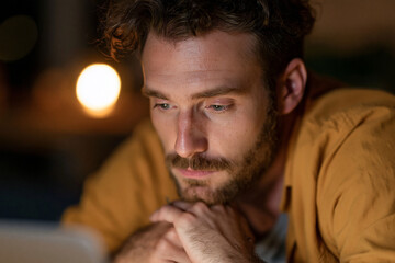 Fototapeta premium Man rests fingers near tablet screen. Focused gaze suggests deep thought or concentration. Soft lighting highlights his calm, contemplative expression. Ideal for scenes of study, planning