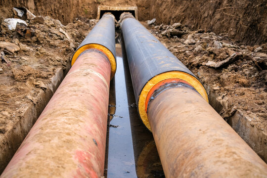 Excavated trench with old worn heating pipes and new insulated pipeline section during repair maintenance infrastructure concept