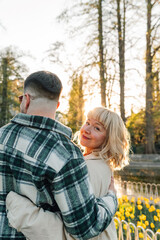 Fototapeta premium Couple embracing in park at golden hour, woman smiling back at camera, enjoying spring romance