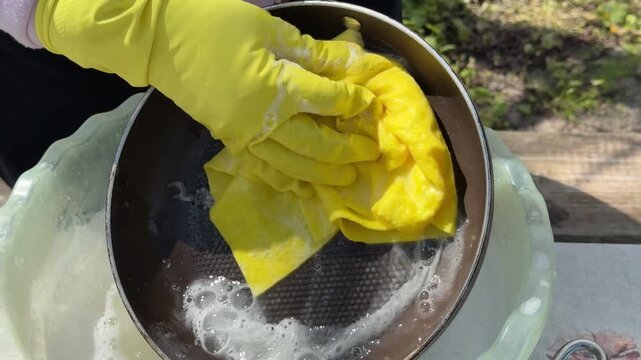 A woman in yellow gloves washes a frying pan with a yellow rag and a winterizing agent.
