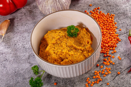 Spicy red lentil dip in bowl with fresh bell pepper garlic and chili on grey background