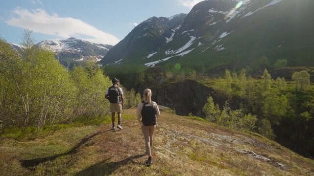 A hiking couple pauses in a breathtaking mountain landscape to rest, remove backpacks and sweaters, then continue their outdoor wilderness adventure.