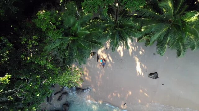 Aerial rocket shot revealing a couple lying on the white sands of Sunset Beach, Seychelles, framed by coconut palms and turquoise waves, 30fps 003 1080p