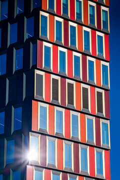 Colorful facade with red and blue windows forming a geometric pattern across a modern tower exterior with sunlight reflection and urban design detail