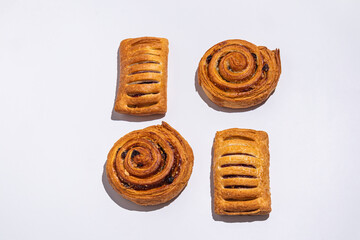 Fototapeta premium fresh pastries. Four buns with fruit filling, puffs and round cinnamon snails on a white background. A pastry mockup to advertise your product.