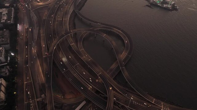Aerial view of the Coastal Road interchange featuring complex overpasses and traffic with headlights at dusk near the water in Mumbai, Maharashtra, India.