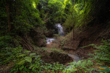 A turquoise waterfall cascades down in layers in the middle of the forest. © Pongsorn