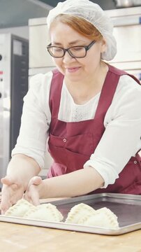 Adult kind smiling woman bakes and forming pies in the bakery
