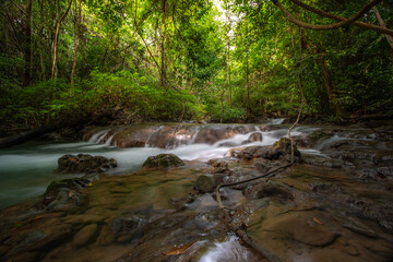 A turquoise waterfall cascades down in layers in the middle of the forest. © Pongsorn