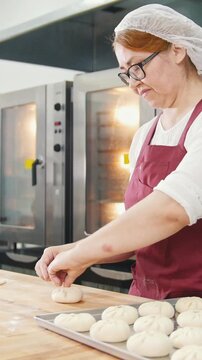 Adult kind smiling woman bakes and forming meat pies in the bakery