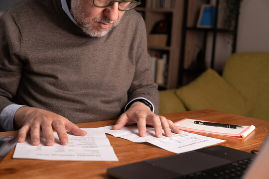 Senior man reviewing bills and financial documents at home making budget decisions