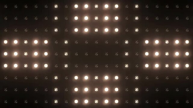 Flashing warm white LED light bulbs on a dark grid panel forming an abstract cross pattern, stage lighting concert backdrop.