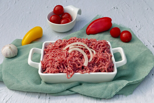 Frisches Rinderhackfleisch in einer wei&szlig;en Auflaufform, mit Zwiebelringen und Gem&uuml;se.