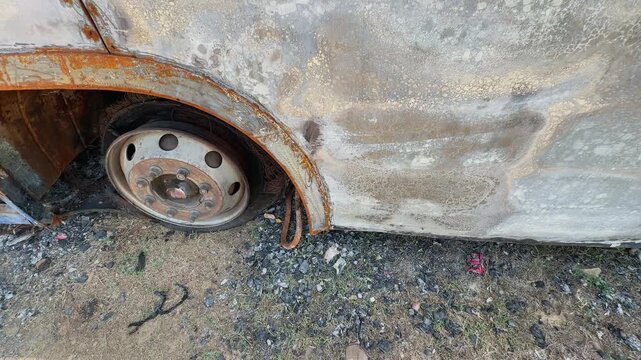 Closeup shot of a fire damaged sleeper bus wheel area with scorched body panels, melted tire remains, rusted wheel rim and ash covered roadside ground!