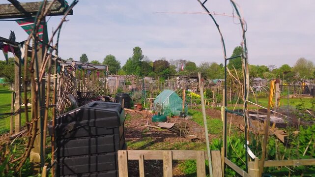 Approaching low angle perspective moves through a metal garden archway into a rustic cultivation plot. The garden features weathered wooden fencing colorful bunting hanging from a timber trellis and a