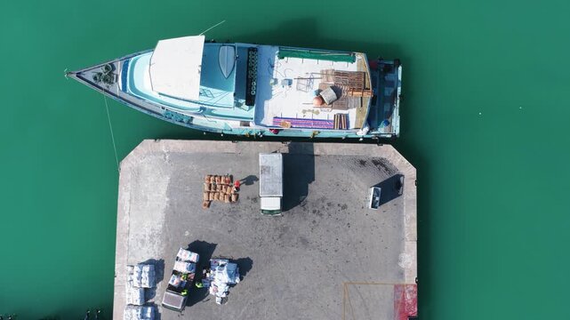 Aerial view of a traditional boat docked at a concrete pier with cargo sacks and a small truck on the turquoise water Kudahuvadhoo, Dhaalu Atoll, Maldives.