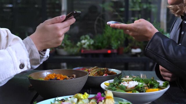 Unrecognizable people using a mobile phone and credit card for a contactless payment while having lunch at a modern vegan restaurant, splitting the bill for their healthy meal