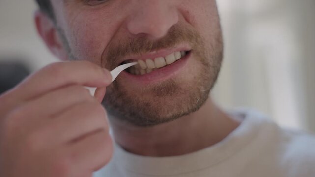 Close up of a man using a floss pick to clean his teeth, maintaining oral health and hygiene