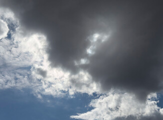 Obraz premium Dark storm cloud covers a blue sky. Sunlight breaks through the cloudscape with bright edges. Weather background for nature and atmosphere..