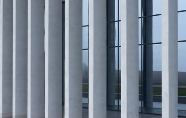 Naklejka premium Modern building facade with tall vertical columns and glass windows. Minimalist architecture with gray exterior lines and reflective surfaces. Ideal