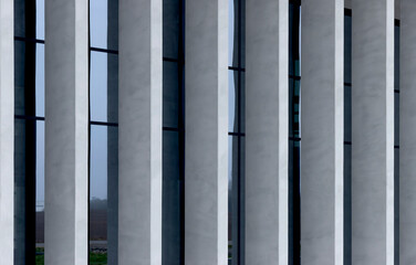 Naklejka premium Modern building facade with vertical concrete fins and dark window panels. Geometric exterior lines create a clean architectural pattern. Suitable for