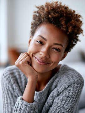 Portrait of a beautiful young Black woman with short curly hair resting her chin on hand with a serene smile.