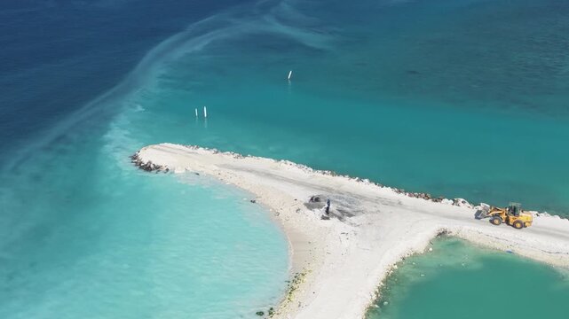 Aerial view of a sand breakwater construction with a yellow loader in turquoise waters Kudahuvadhoo, Dhaalu Atoll, Maldives.