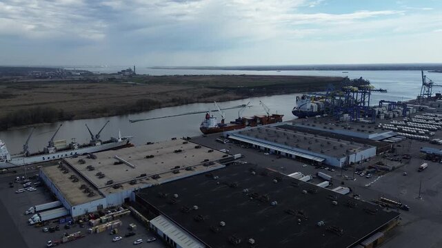 Container ship vessel berth. Cargo activity spans Christina River at Port Wilmington docked beside warehouse rows along River Road. Bright metal roofs, stacked containers shape textures, DE