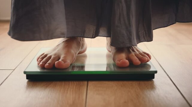 Close up person legs bare feet stepping onto weighing scale at home room. Fitness diet BMI girl slimming healthy lifestyle weight awareness concept. Woman weight lose standing on scales measure weight