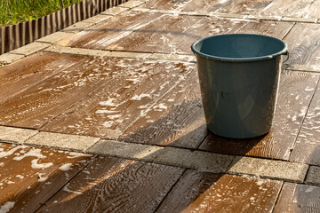 Naklejka premium Washing the paving slabs on the terrace in front of the house in the garden, a bucket with hot water and detergent, water with detergent spilled on the tiles to remove dirt from the tiles,