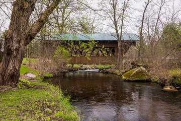 Fototapeta premium A Covered Bridge Crossing A River During Spring
