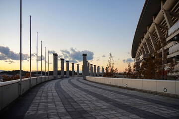 Fototapeta premium Curved Pedestrian Walkway Beside a Modern Stadium at Sunset
