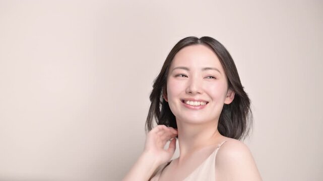 ベージュ背景の風になびくサラサラ黒髪と笑顔の女性美肌と透明感あるスキンケア美容やトリートメントイメージ髪をかき上げる動画　スローモーション