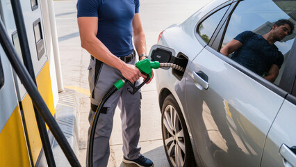 man filling gas tank, Attendant refueling silver car with gas. Man holding green fuel pump nozzle. Service worker filling silver sedan tank. Close-up of fueling at petrol station. © Jakub