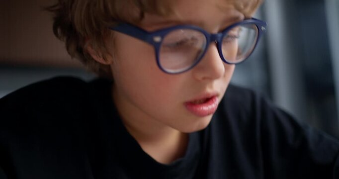 Focused Boy Examining Workbook Closely. Pensive Child Studying Intently Under Warm Kitchen Lighting