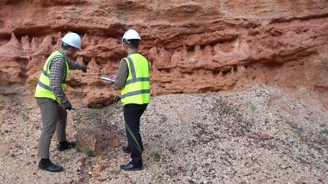 Two geologists analyzing soil and rock formations at a mining excavation site. They are conducting geological surveys and evaluating mineral resources for industrial project planning.