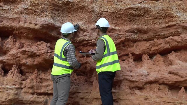 Two geologists analyzing soil and rock formations at a mining excavation site. They are conducting geological surveys and evaluating mineral resources for industrial project planning.