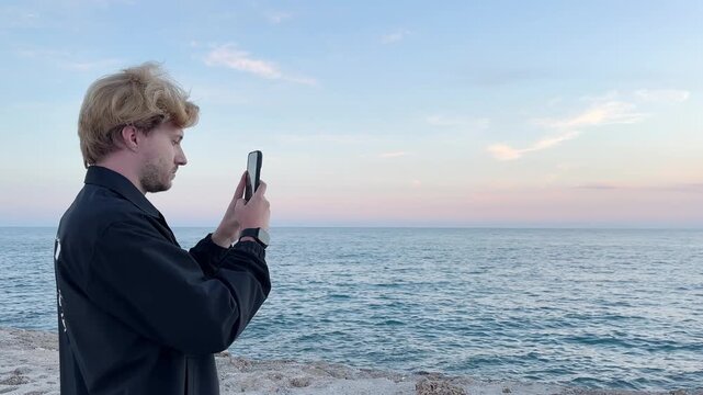 young man walking along the promenade and taking pictures.uses a smartphone