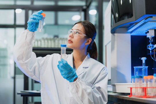 Asian female scientist holding and comparing two sample tubes for clinical testing in lab.
