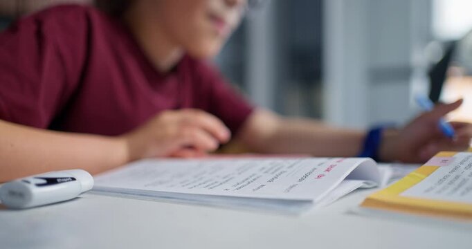 Young Boy Concentrates On Workbook Tasks With Precise Hand Movements In Welllit Kitchen Environment