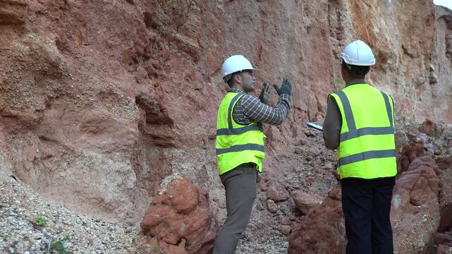 Two geologists analyzing soil and rock formations at a mining excavation site. They are conducting geological surveys and evaluating mineral resources for industrial project planning.