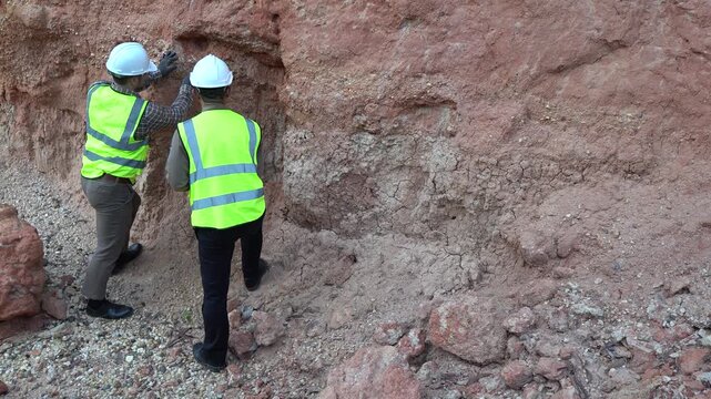 Two geologists analyzing soil and rock formations at a mining excavation site. They are conducting geological surveys and evaluating mineral resources for industrial project planning.